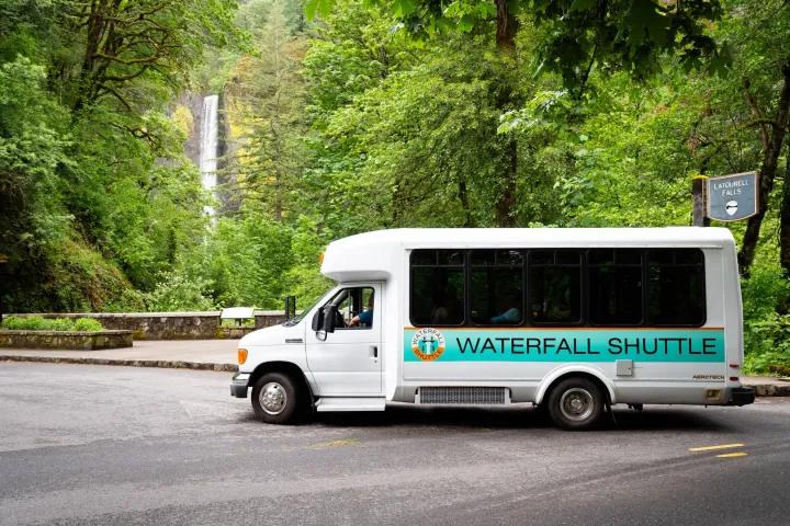 a bus is parked on the side of a road with trees and waterfall
