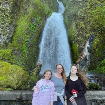 Three people standing in front of a large waterfall surrounded by lush green moss.