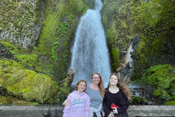 Three people standing in front of a large waterfall surrounded by lush green moss.