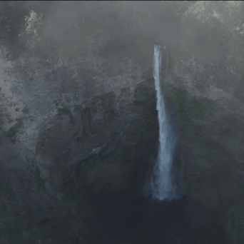 Tall waterfall cascading into deep, misty gorge surrounded by forest.