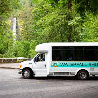 White shuttle bus parked near forest with waterfall and Latourell Falls sign.
