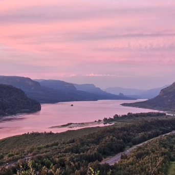 River bend with hills at sunset, pink and purple sky reflected on water.
