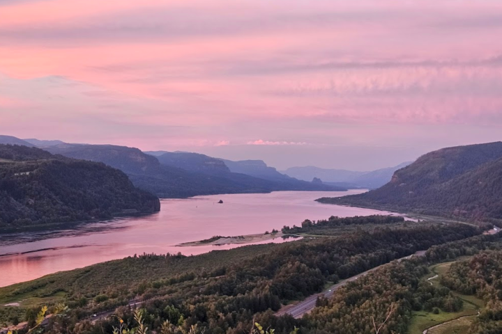 River bend with hills at sunset, pink and purple sky reflected on water.
