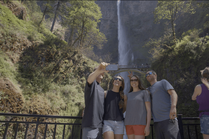 Group of people taking a selfie with a large waterfall in the background.