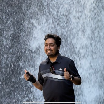 Smiling person giving thumbs up in front of a waterfall.