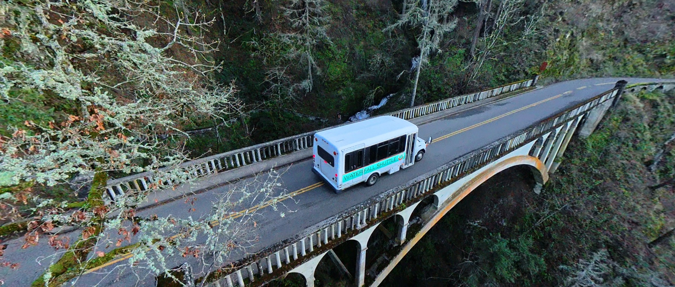Shuttle bus crossing a narrow bridge surrounded by forest.