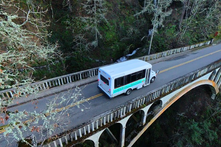 Shuttle bus crossing a narrow bridge surrounded by forest.