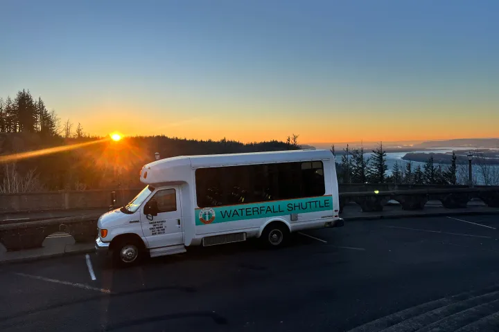 White shuttle bus parked at sunset with distant river and trees in background.