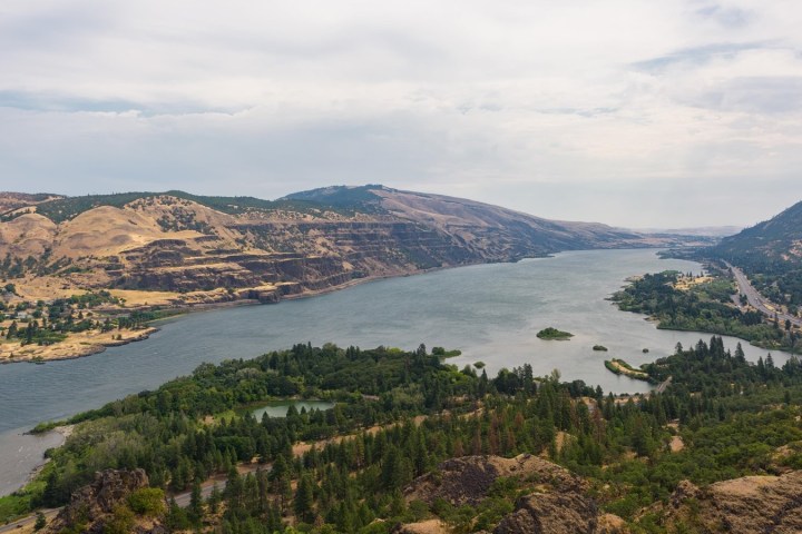 River winding through hills with green trees and cloudy sky.