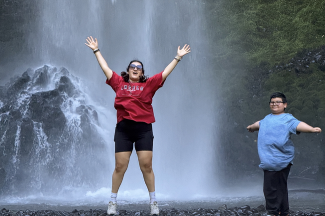 Two people in front of a waterfall; one jumping, both smiling.
