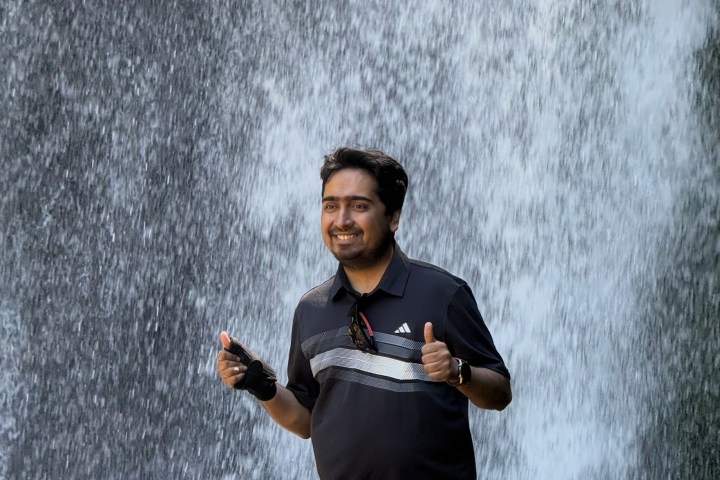 Smiling person giving thumbs up in front of a waterfall.