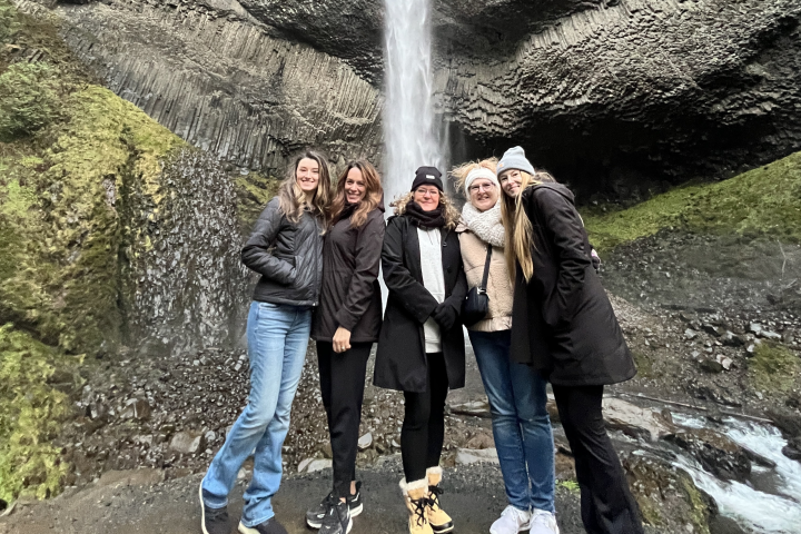 Five people in winter clothing stand smiling in front of a tall waterfall.
