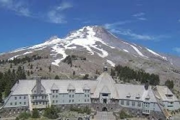 Large lodge with mountain backdrop, partly covered in snow under clear blue sky.