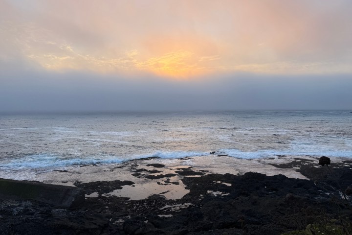 Ocean view with rocky coast at sunset, sky transitioning from orange to blue.