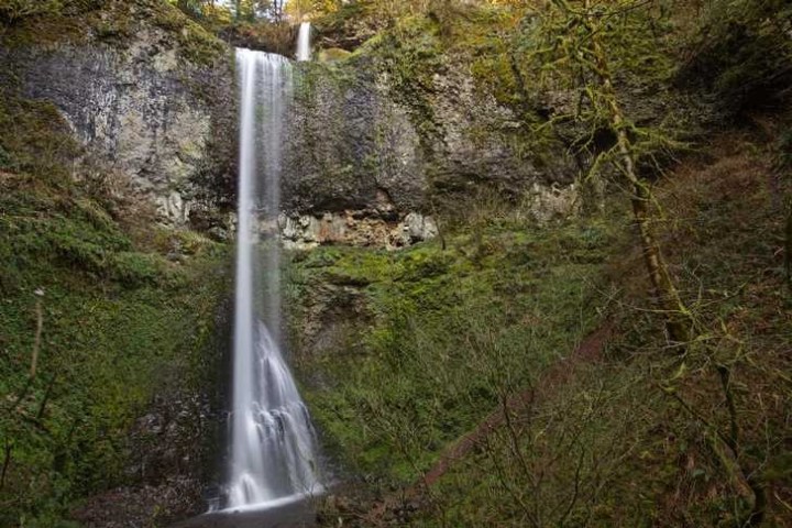 Tall waterfall cascading over a cliff surrounded by lush greenery.