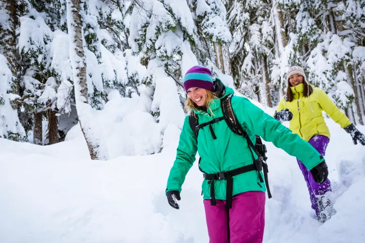 Two mt hood people in colorful winter gear hiking through a snowy forest.